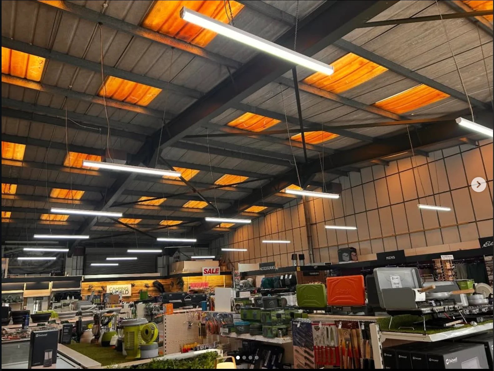 Large warehouse with orange and black metal grid ceiling, industrial lighting, and various equipment and tools displayed on the floor below